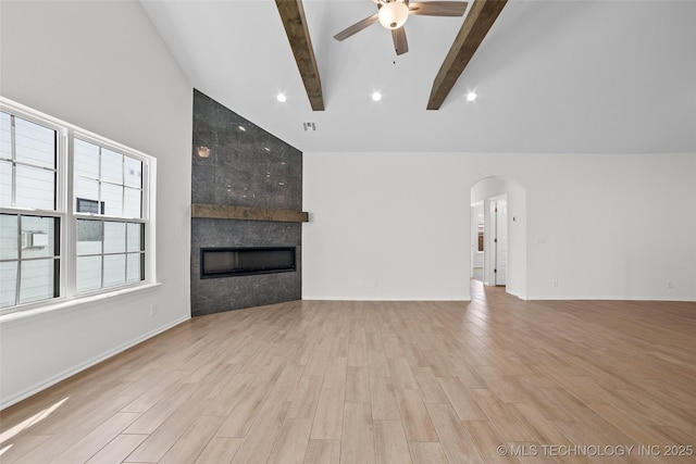 unfurnished living room with high vaulted ceiling, a fireplace, light wood-type flooring, ceiling fan, and beam ceiling