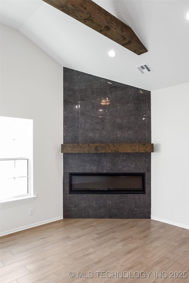 unfurnished living room with a tiled fireplace, vaulted ceiling, and wood-type flooring