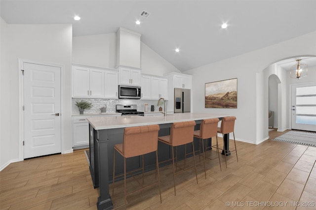 1941 W Huntsville Pl, Broken Arrow, OK 74011 - kitchen featuring appliances with stainless steel finishes, arched walkways, a center island with sink, white cabinetry, and high vaulted ceiling
