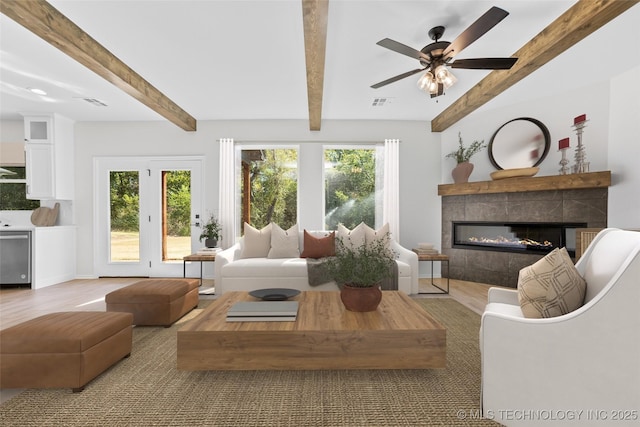 living room featuring beamed ceiling, a healthy amount of sunlight, and a tiled fireplace