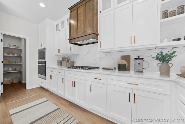 kitchen featuring premium range hood, appliances with stainless steel finishes, tasteful backsplash, white cabinetry, and light hardwood / wood-style flooring