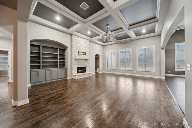 unfurnished living room featuring dark wood-type flooring, a towering ceiling, coffered ceiling, a fireplace, and a chandelier