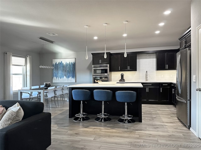 kitchen with appliances with stainless steel finishes, tasteful backsplash, a kitchen bar, hanging light fixtures, and a center island with sink