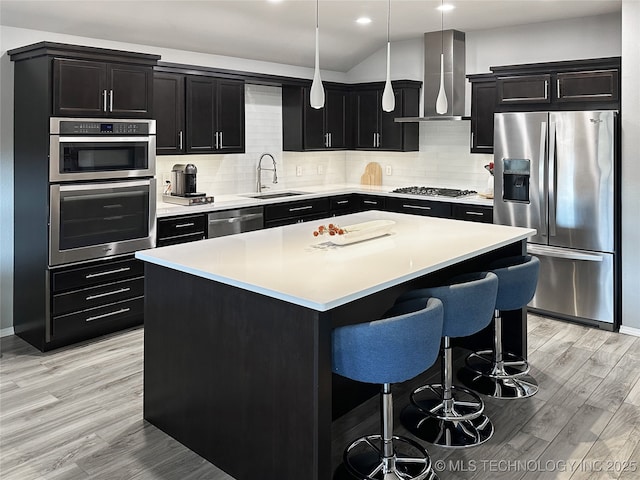 kitchen with sink, a center island, pendant lighting, stainless steel appliances, and wall chimney range hood