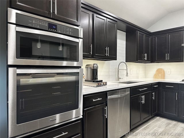 kitchen featuring appliances with stainless steel finishes, lofted ceiling, sink, backsplash, and light hardwood / wood-style flooring