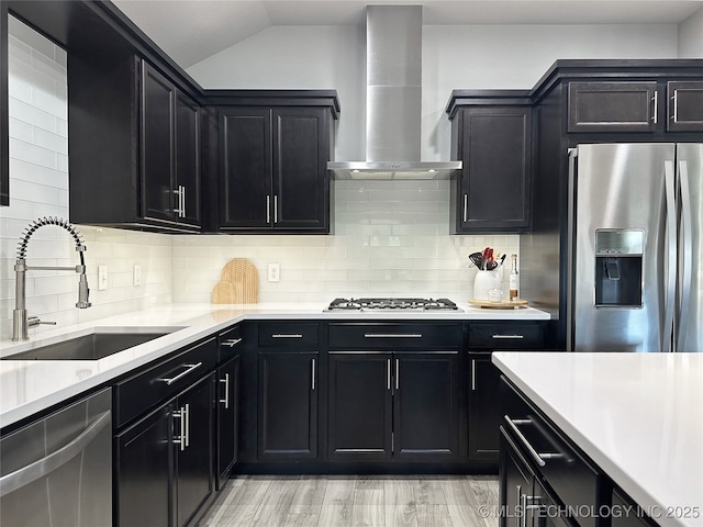 kitchen with wall chimney range hood, sink, stainless steel appliances, decorative backsplash, and vaulted ceiling