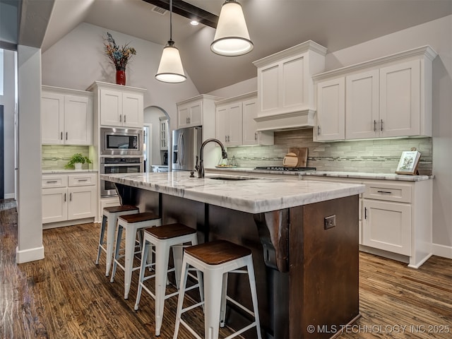 kitchen with white cabinetry, decorative light fixtures, stainless steel appliances, light stone countertops, and a kitchen island with sink