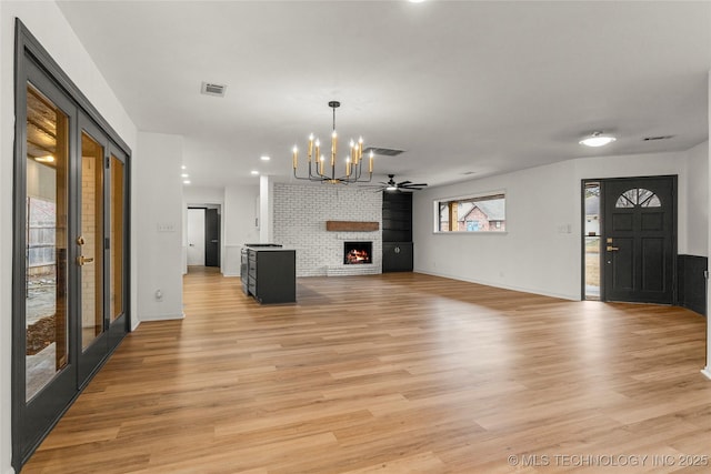 unfurnished living room featuring light wood-type flooring, ceiling fan with notable chandelier, a fireplace, and french doors