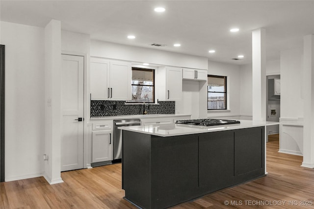 kitchen with appliances with stainless steel finishes, white cabinetry, a center island, light hardwood / wood-style floors, and decorative backsplash