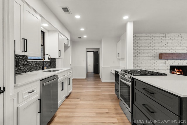 kitchen with sink, appliances with stainless steel finishes, white cabinetry, backsplash, and light wood-type flooring