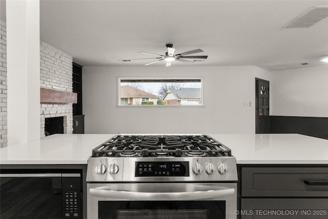 kitchen featuring ceiling fan, kitchen peninsula, gas stove, and a brick fireplace