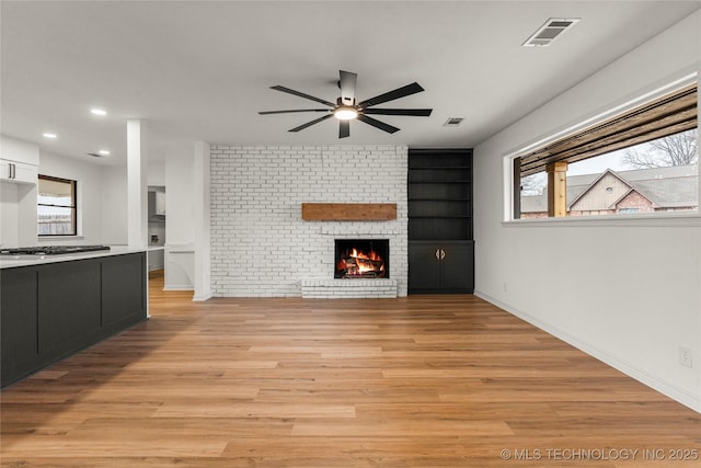 unfurnished living room with ceiling fan, a brick fireplace, built in features, and light hardwood / wood-style floors