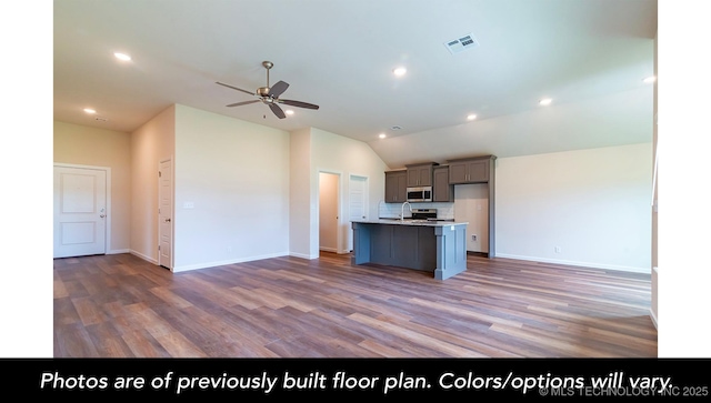 kitchen featuring wood-type flooring, appliances with stainless steel finishes, a kitchen island with sink, and lofted ceiling