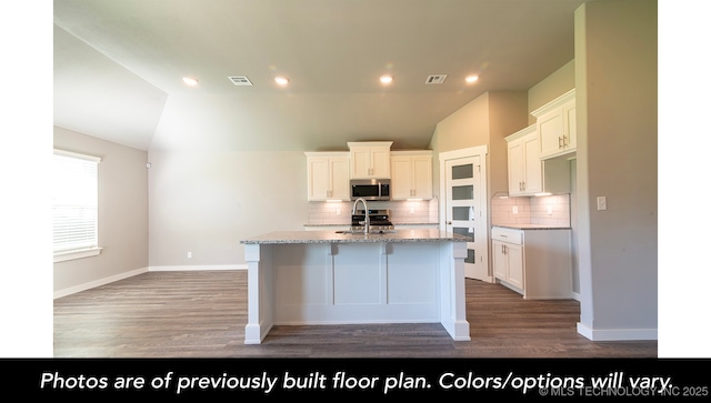 kitchen with white cabinetry, sink, light stone countertops, and an island with sink