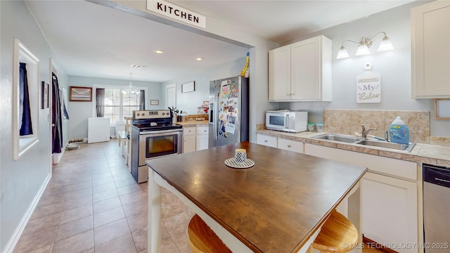 kitchen featuring pendant lighting, sink, light tile patterned floors, stainless steel appliances, and white cabinets