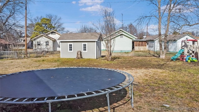 back of house featuring a trampoline, a yard, an outdoor structure, and a playground