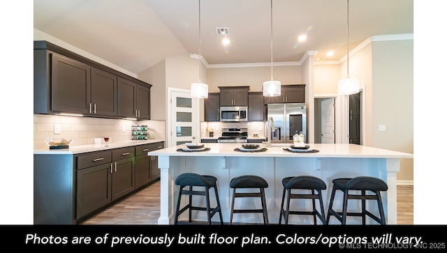 kitchen featuring appliances with stainless steel finishes, decorative light fixtures, a kitchen island with sink, dark brown cabinetry, and light wood-type flooring