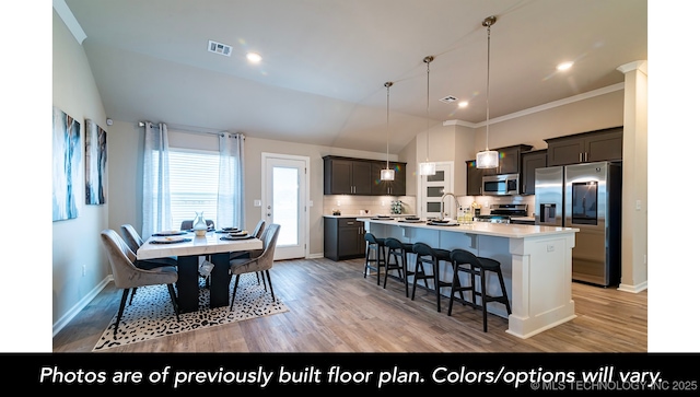 kitchen featuring pendant lighting, appliances with stainless steel finishes, tasteful backsplash, an island with sink, and light wood-type flooring