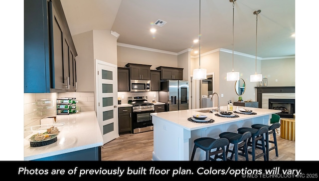 kitchen with a kitchen bar, sink, an island with sink, pendant lighting, and stainless steel appliances