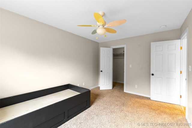 unfurnished bedroom featuring light carpet, a walk in closet, a closet, and ceiling fan