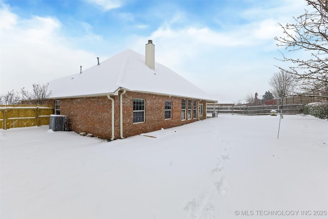 snow covered rear of property featuring central AC