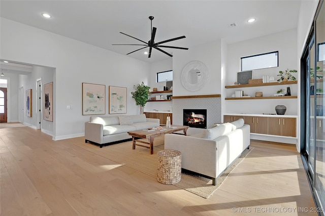 living room featuring ceiling fan, a healthy amount of sunlight, a tiled fireplace, and light hardwood / wood-style floors