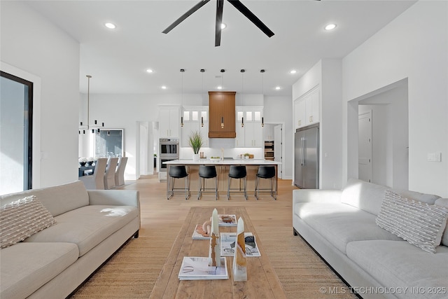 living room with ceiling fan, sink, and light wood-type flooring