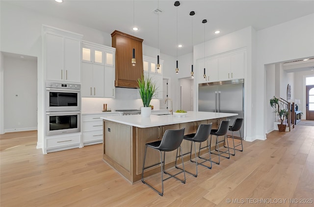 kitchen featuring light hardwood / wood-style flooring, appliances with stainless steel finishes, white cabinetry, an island with sink, and decorative light fixtures