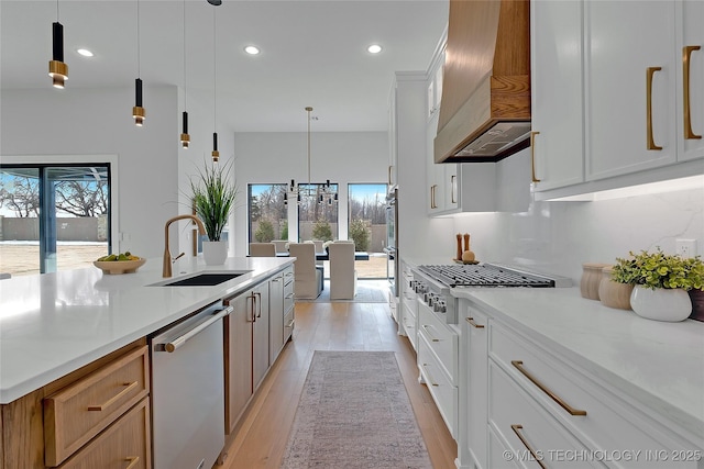 kitchen with sink, white cabinets, custom exhaust hood, hanging light fixtures, and stainless steel appliances