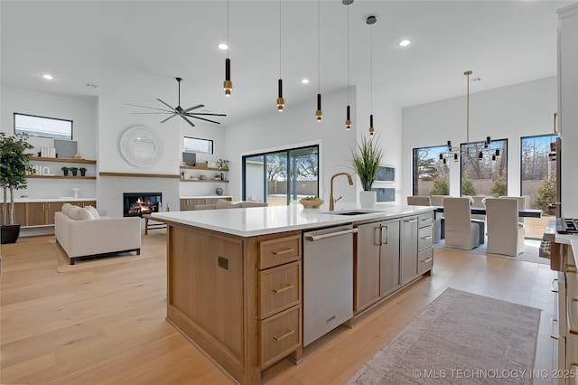 kitchen featuring sink, hanging light fixtures, light wood-type flooring, an island with sink, and a tiled fireplace