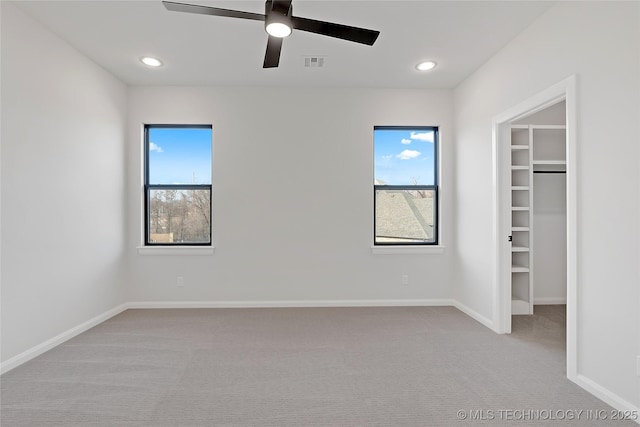 unfurnished bedroom with multiple windows, a walk in closet, light carpet, and ceiling fan