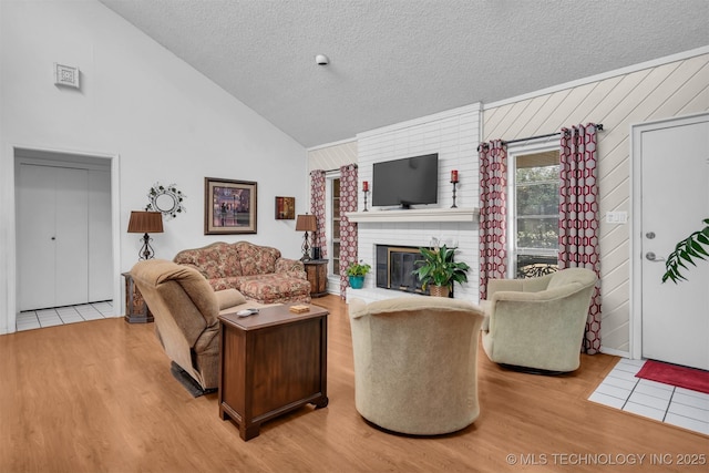 living room with a fireplace, high vaulted ceiling, a textured ceiling, and light wood-type flooring