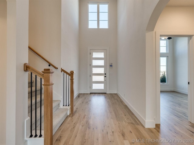 entryway with light wood-style floors, arched walkways, baseboards, and a high ceiling