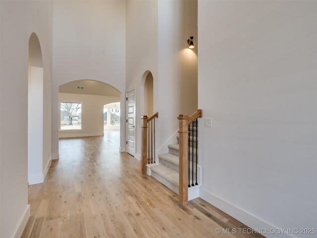 hall with arched walkways, a high ceiling, baseboards, and light wood-style floors