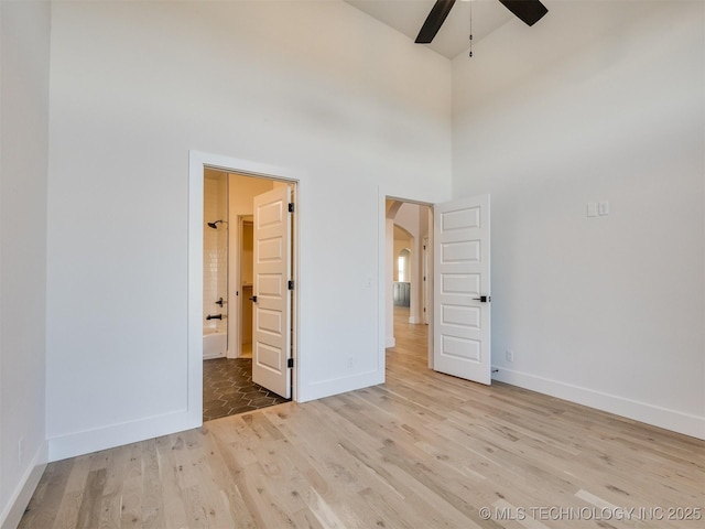 unfurnished bedroom with a towering ceiling, connected bathroom, and light hardwood / wood-style floors