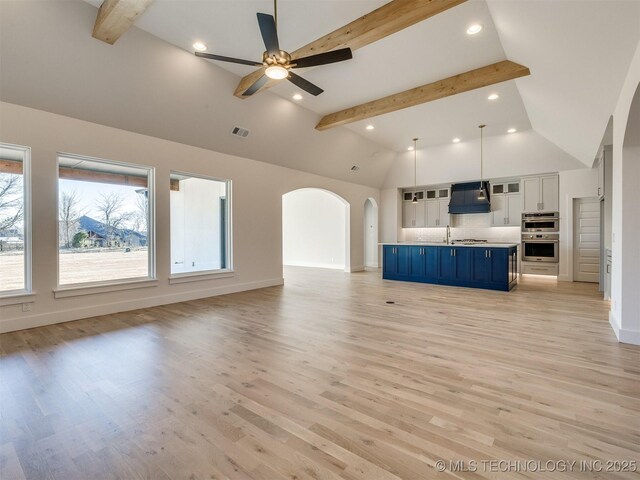 unfurnished living room with ceiling fan, high vaulted ceiling, beam ceiling, and light hardwood / wood-style floors