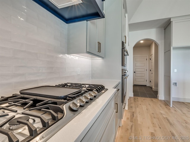 kitchen with arched walkways, extractor fan, stainless steel appliances, light wood-type flooring, and backsplash