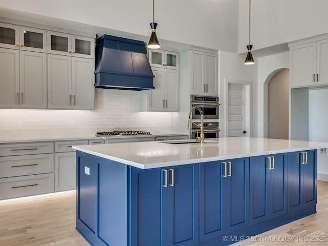 kitchen featuring custom exhaust hood, blue cabinetry, a center island with sink, and decorative light fixtures