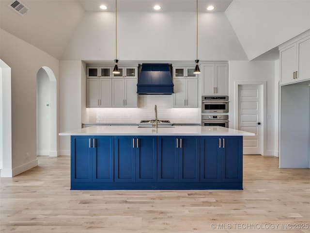 kitchen featuring pendant lighting, premium range hood, white cabinetry, high vaulted ceiling, and an island with sink