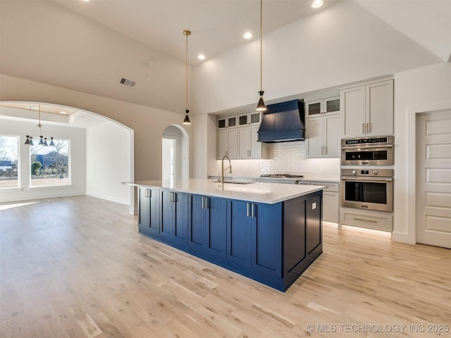 kitchen featuring appliances with stainless steel finishes, decorative light fixtures, sink, white cabinets, and custom range hood