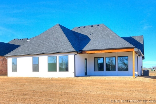 rear view of property with stucco siding, roof with shingles, cooling unit, and a yard