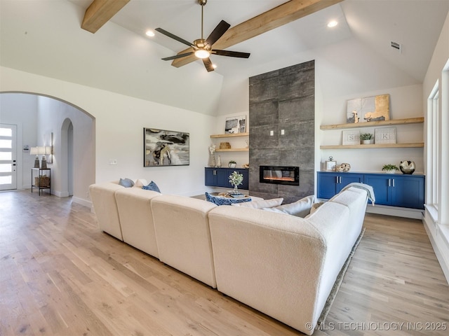 2508 E 135th Dr S, Bixby, OK 74008 - living area featuring arched walkways, high vaulted ceiling, a tiled fireplace, a ceiling fan, and light wood-type flooring
