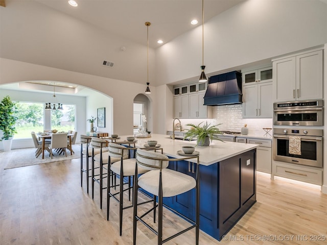 2508 E 135th Dr S, Bixby, OK 74008 - kitchen featuring custom exhaust hood, appliances with stainless steel finishes, high vaulted ceiling, light wood-type flooring, and arched walkways