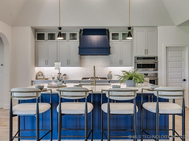 2508 E 135th Dr S, Bixby, OK 74008 - kitchen featuring premium range hood, appliances with stainless steel finishes, backsplash, vaulted ceiling, and an island with sink