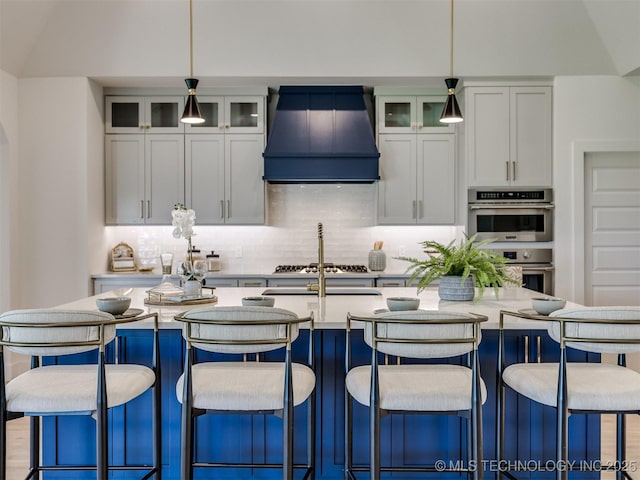 2508 E 135th Dr S, Bixby, OK 74008 - kitchen with premium range hood, stainless steel double oven, tasteful backsplash, an island with sink, and pendant lighting
