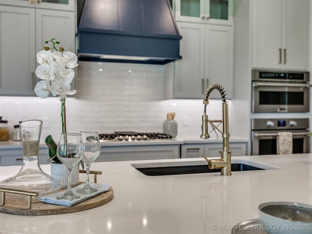 2508 E 135th Dr S, Bixby, OK 74008 - kitchen with custom exhaust hood, a sink, stainless steel double oven, backsplash, and glass insert cabinets