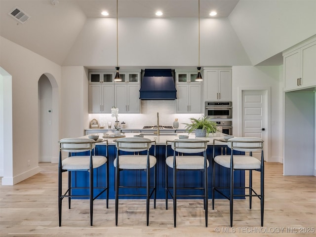 2508 E 135th Dr S, Bixby, OK 74008 - kitchen with premium range hood, double oven, arched walkways, high vaulted ceiling, and decorative backsplash
