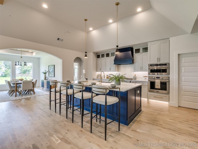 2508 E 135th Dr S, Bixby, OK 74008 - kitchen with premium range hood, double oven, high vaulted ceiling, arched walkways, and light wood-style flooring