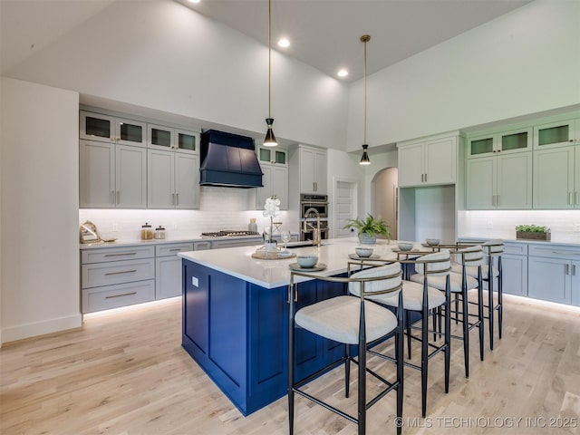 2508 E 135th Dr S, Bixby, OK 74008 - kitchen with custom range hood, high vaulted ceiling, decorative backsplash, light wood-style flooring, and a large island with sink