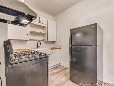 kitchen with black refrigerator, range with gas stovetop, tasteful backsplash, white cabinets, and exhaust hood